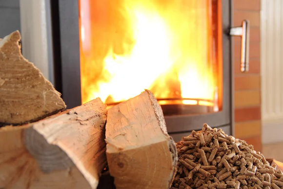 Holzscheite und Holzpellets vor brennendem Kamin.